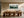Framed misty pine forest watercolor displayed above a long wooden dining table and sculptural chairs.