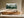 Framed misty pine forest watercolor hanging above a long wooden sideboard in sunlit space.