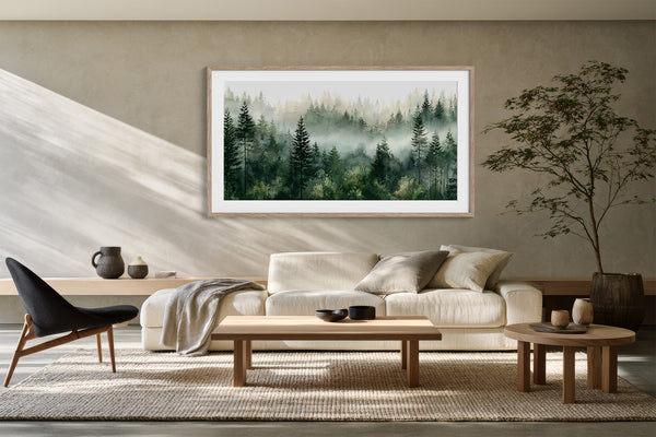 Large framed misty pine forest watercolor above a cream sofa, with wood tables and chair.