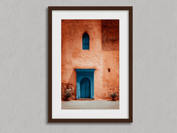 Framed Moroccan street scene art print featuring a vivid blue doorway and ochre wall. A soulful, timeless piece for eclectic interiors.