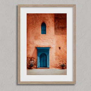 Framed Moroccan street scene art print featuring a vivid blue doorway and ochre wall. A soulful, timeless piece for eclectic interiors.