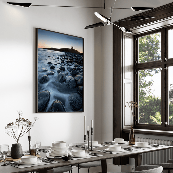 Framed fine art print of Northumbrian castle ruins at sunrise, with glowing rocks, tranquil sea, and lingering moonlight in soft dawn hues.