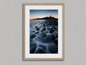 Framed Dunstanburgh Castle sunrise wall art print with a Northumberland boulder shore