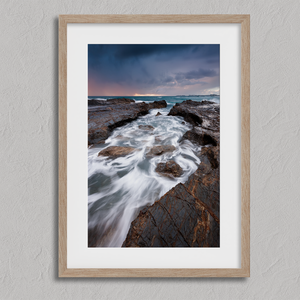 Framed wall art of the Australian coast with rugged rocks, azure sea, and moody skies. A striking coastal landscape print. Ready to hang.