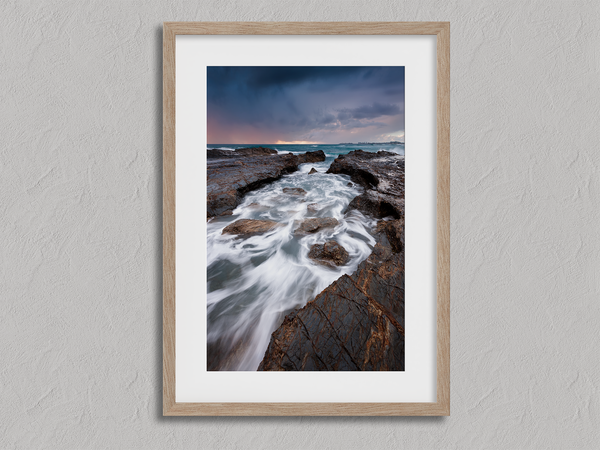 Framed wall art of the Australian coast with rugged rocks, azure sea, and moody skies. A striking coastal landscape print. Ready to hang.