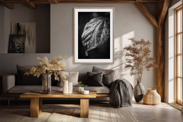 Framed black-and-white wet leaf photograph above a dark sofa and wooden coffee table.