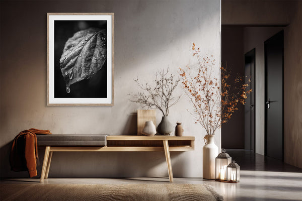 Framed wet leaf photograph above a wooden console table with vases in a hallway.