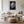 Framed monochrome wet leaf artwork above a white sofa, wood coffee table, and round ottoman.