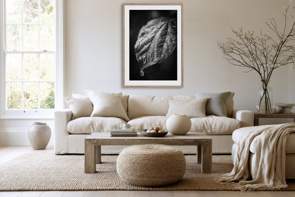 Framed monochrome wet leaf artwork above a white sofa, wood coffee table, and round ottoman.
