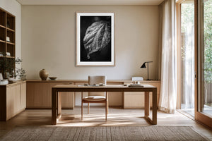 Framed monochrome leaf photograph above a wooden desk with a chair and table lamp.