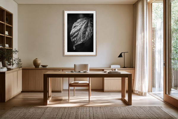 Framed monochrome leaf photograph above a wooden desk with a chair and table lamp.