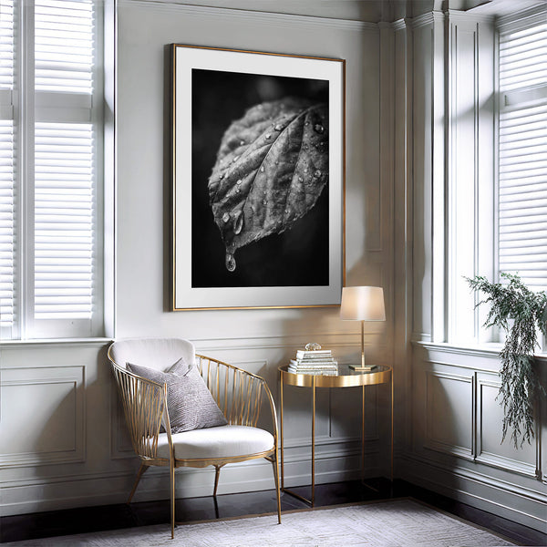 Gold-trimmed framed wet leaf photograph above a gold chair and small round side table.