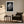 Framed black-and-white rain-covered leaf print above an armchair, side table, and floor lamp.