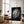 Large black-framed wet leaf artwork leaning against a wall beside an armchair and floor lamp.