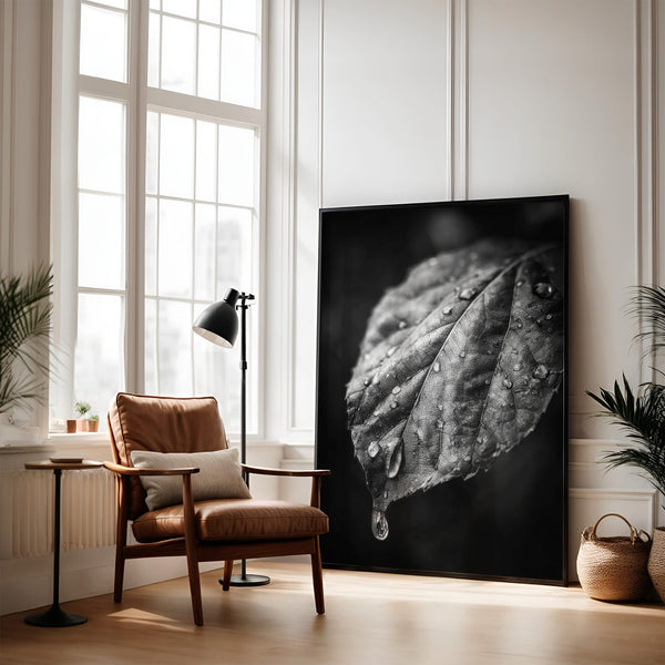 Large black-framed wet leaf artwork leaning against a wall beside an armchair and floor lamp.