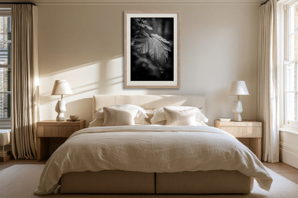 Framed black-and-white rain-covered leaf photograph above a bed between two bedside lamps.