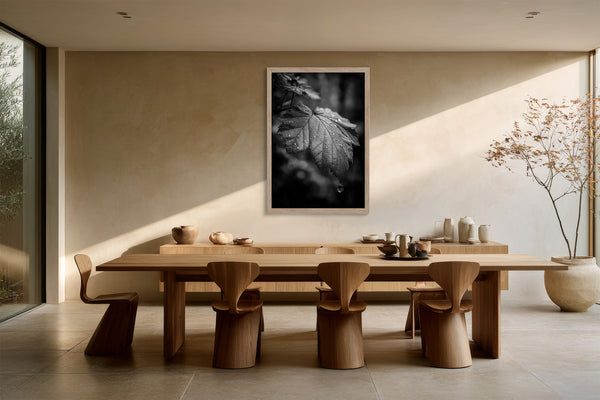 Framed black-and-white rain-covered leaf photograph above a long wooden dining table and sculptural chairs.