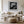Black-framed lighthouse artwork above a white sofa, low wood table, and round woven ottoman.