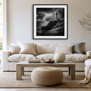 Black-framed lighthouse artwork above a white sofa, low wood table, and round woven ottoman.