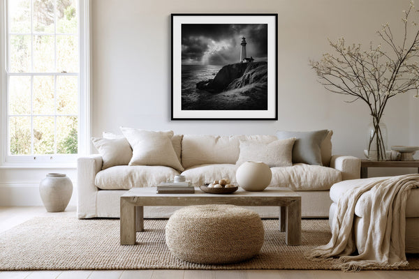 Black-framed lighthouse artwork above a white sofa, low wood table, and round woven ottoman.