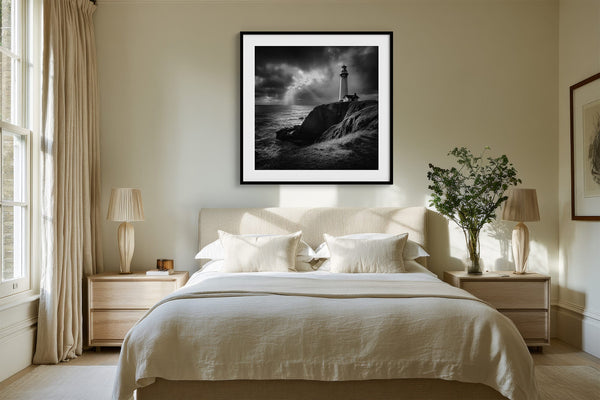 Black-framed lighthouse print centered above a neatly made bed with light wood nightstands.