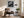 Black-framed lighthouse print above a brown armchair beside a floor lamp and bright windows.