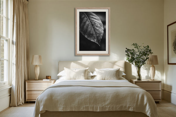 Framed black-and-white leaf vein photograph centered above a bed between wooden nightstands.