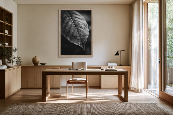 Framed black-and-white leaf vein photograph above a wooden desk with chair and task lamp.