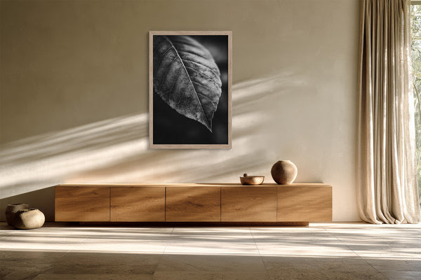 Framed black-and-white leaf vein photograph above a low wooden sideboard with ceramic objects.