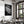 Framed black-and-white dew-covered leaf wall art displayed above a set dining table near tall windows.