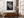Black-and-white leaf wall art in a light frame above a wooden sideboard beside a large window.