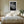 Light-framed dew-covered leaf wall art centered above a bed with white bedding and bedside tables.