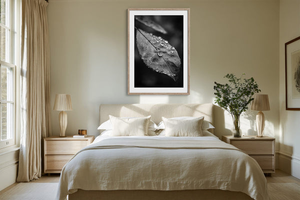 Light-framed dew-covered leaf wall art centered above a bed with white bedding and bedside tables.
