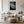Light-framed black-and-white leaf wall art above a cream sofa, coffee table, and woven ottoman.