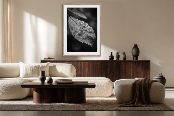Light-framed dew-covered leaf wall art above a curved sofa and dark wooden sideboard.