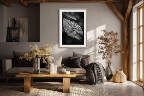 Light-framed black-and-white leaf wall art above a dark sofa in a room with exposed wood beams.