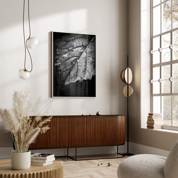 Black-and-white leaf artwork in a light frame above a ribbed wood sideboard.