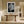 White-matted monochrome leaf artwork above a rustic wood console in a sunlit hallway.