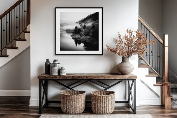 Black-framed misty river artwork above a wood-and-metal console beside a staircase.