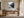 Black-framed Mistwater Valley print above a wooden desk near tall glass doors.