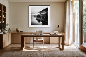 Black-framed Mistwater Valley print above a wooden desk near tall glass doors.