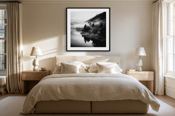 Black-framed misty river artwork above a cream bed between matching bedside lamps.