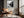 Black-framed river print above a leather lounge chair beside a sunlit window.