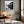 Black-framed river print above a leather lounge chair beside a sunlit window.