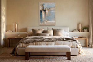Framed blue, beige, and white abstract artwork centered above a bed with neutral linens.