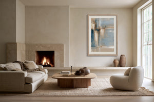 Framed blue and beige abstract artwork displayed above a low ledge near a lit fireplace.