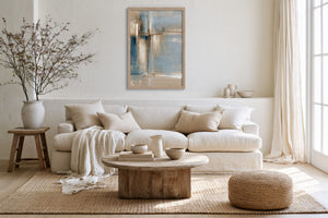 Framed abstract artwork above a white sofa, with a round wood coffee table and woven pouf.