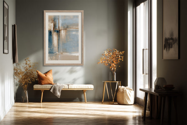 Framed abstract artwork above a cushioned bench with an orange pillow in a sunlit hallway.