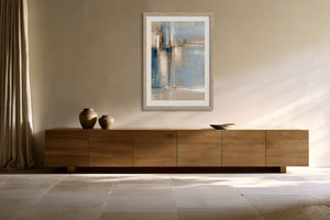 Framed blue and beige abstract artwork above a long wooden sideboard with ceramic vessels.