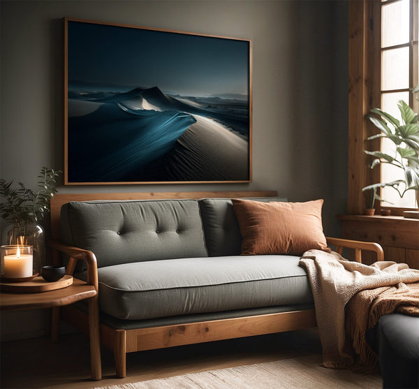 Blue-toned desert dune artwork in a slim wood frame above a gray sofa.